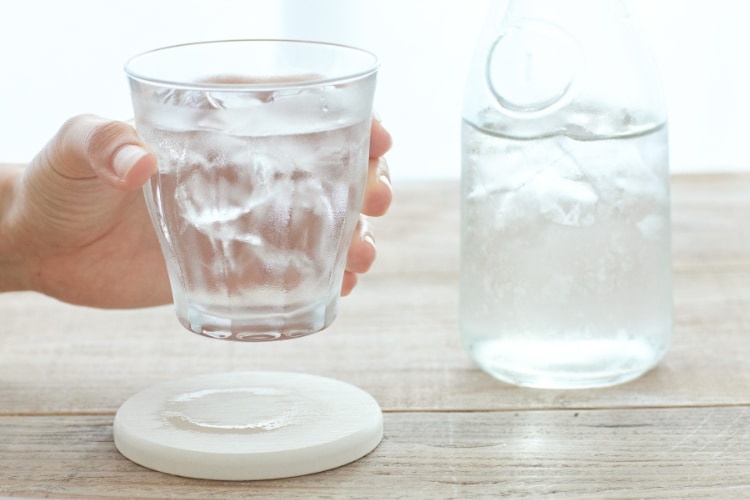 A hand is holding a glass of pure, clean, water with ice cubes in it, next to a pitcher of cold water with ice cubes in it.